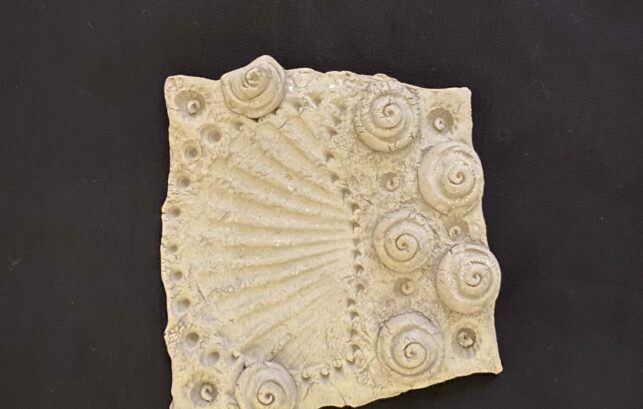 Image shows piece of clay with seashell designs embedded into it.